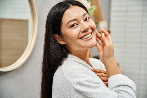 retrato de feliz joven asiático con acné propenso piel de pie en moderno cuarto de baño y mirando a la cámara - Foto, Imagen