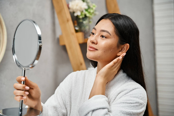 morena e jovem asiático mulher com acne-propenso pele olhando para espelho no moderno banheiro, cuidados com a pele - Foto, Imagem