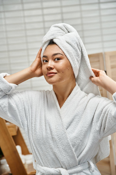 Kafasında beyaz havlu olan genç Asyalı kadın banyoda kameraya bakıyor, deri sorunları var. - Fotoğraf, Görsel