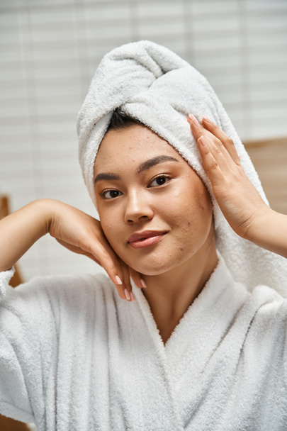 tiro vertical de mujer asiática joven con piel propensa al acné con toalla blanca en la cabeza en el baño - Foto, imagen