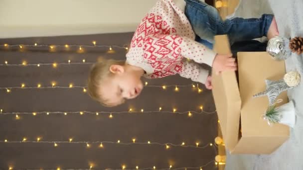 Pieni kaksivuotias poika avaa joululahjoja kotona. - Materiaali, video
