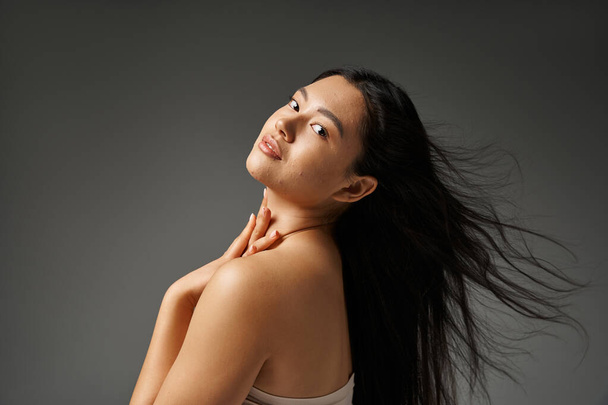 junge asiatische Frau mit brünetten Haaren und zu Akne neigender Haut beim Anblick des Spiegels im Badezimmer, Banner - Foto, Bild