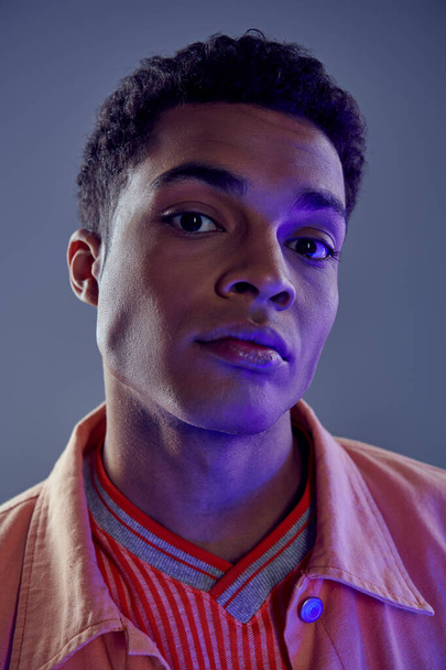 Şeftali rengi gömlekli yakışıklı Afro-Amerikalı adamın portresi gri ışıkta mavi ışıkta kameraya bakıyor. - Fotoğraf, Görsel