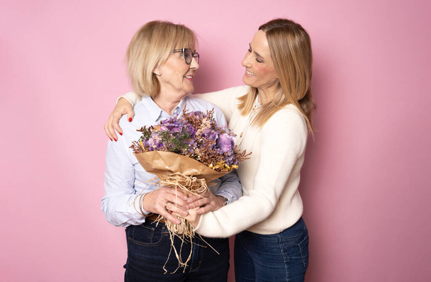 Trendy attractive cheerful mother and daughter enjoying holiday together having big flawless seasonal colorful bouquet of tulips, comfort pleasure joy enjoyment concept isolated on pink background - Photo, Image