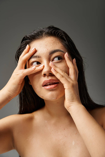 giovane donna asiatica con capelli castani e pelle incline all'acne guardando specchio in bagno, banner - Foto, immagini