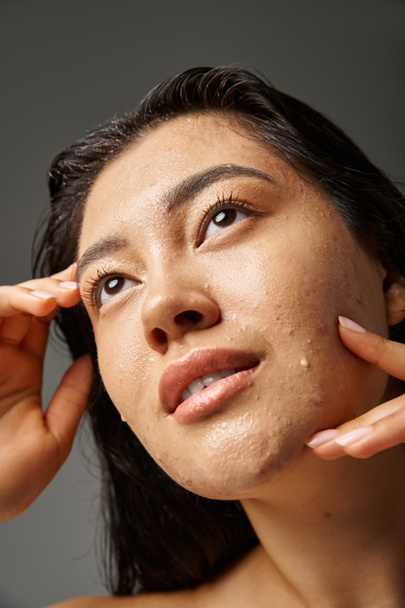 mujer asiática joven con pelo morena y piel propensa al acné mirando el espejo en el baño, pancarta - Foto, imagen