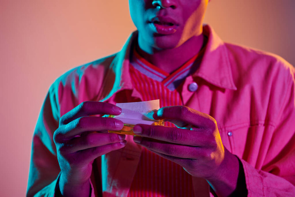 ritagliato africano americano uomo rotolamento sigaretta su sfondo vibrante con illuminazione al neon blu - Foto, immagini