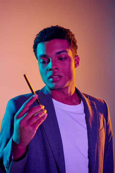ハンサムな若いアフリカ系アメリカ人男性,青いネオンライトの下にタバコを保持しています ピンクの背景 - 写真・画像