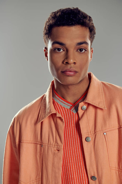 young african american man in peach color shirt looking at camera on grey backdrop, gen z fashion - Φωτογραφία, εικόνα