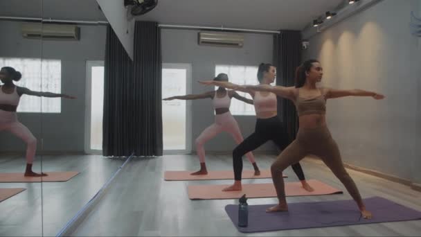 Ευρεία βολή των πολυεθνικών γυναικών yogis εξάσκηση πολεμιστής θέτουν κατά τη διάρκεια της τάξης στο ευρύχωρο στούντιο, αντιγραφή χώρου - Πλάνα, βίντεο