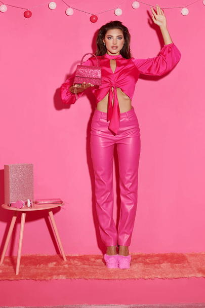クロップトップの女性のような華やかな人形とボールガーランド近くのハンドバッグと立っているピンクのズボン - 写真・画像