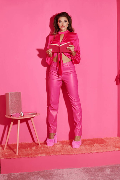 ευτυχισμένη κούκλα σαν γυναίκα σε crop top και ροζ παντελόνι στέκεται με το βιβλίο και κοιτάζοντας κάμερα - Φωτογραφία, εικόνα