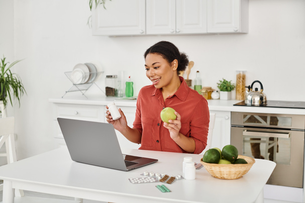 リンゴとサプリメントを保持しているアフリカ系アメリカ人の栄養士は,オンラインで健康に関するアドバイスを提供しながら - 写真・画像