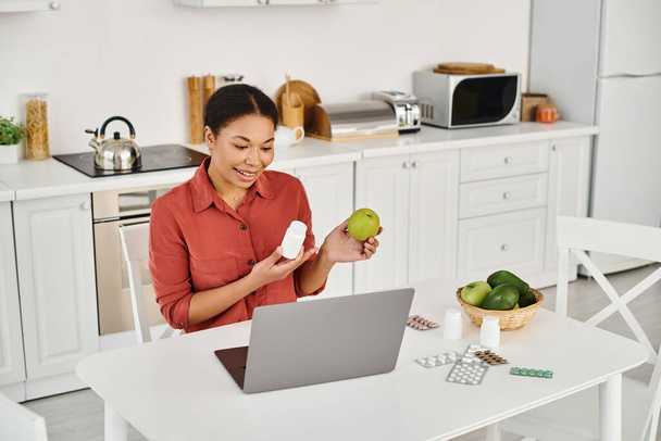 african american nutritionist holding apple and supplements while giving diet advice online - Photo, Image