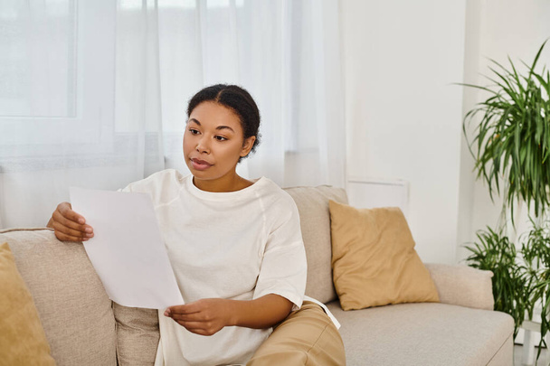 brunette african american woman in casual attire reading dietary prescription and relaxing on sofa - Photo, Image