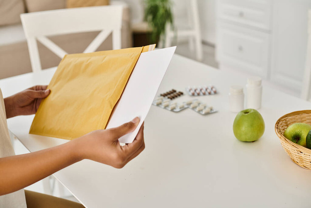 zugeschnittene Ansicht einer schwarzen Frau, die ihren Ernährungsplan überprüft, während sie den Umschlag in der Nähe von Nahrungsergänzungsmitteln öffnet - Foto, Bild