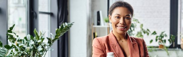 heureux afro-américain diététiste tenant bouteille avec des suppléments et souriant au bureau, bannière - Photo, image