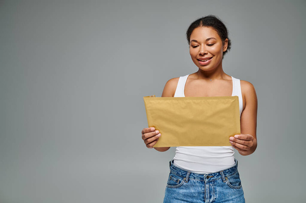 happy african american dietitian holding envelope containing a dietary plan on grey backdrop - Photo, Image
