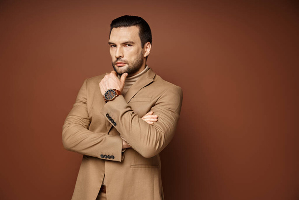 handsome man in elegant attire giving confident look while posing with hand near chin on beige - Photo, Image