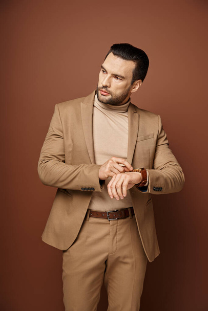 handsome man in elegant attire checking his wristwatch on beige background, time management - Photo, Image