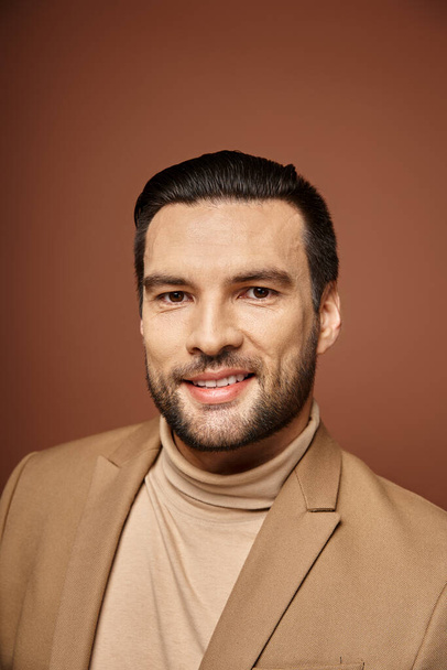portrét atraktivního muže v elegantním oblečení při pohledu na kameru a s úsměvem na béžovém pozadí - Fotografie, Obrázek