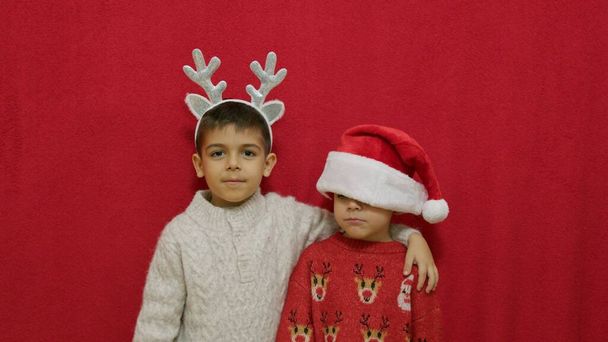 Cute chłopcy bracia ubrani w Boże Narodzenie nosić przytulanie izolacji na czerwonym tle z miejsca kopiowania. Wysokiej jakości zdjęcie - Zdjęcie, obraz