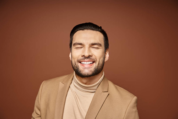 Porträt eines attraktiven Mannes in eleganter Kleidung, der mit geschlossenen Augen auf beigem Hintergrund lächelt - Foto, Bild