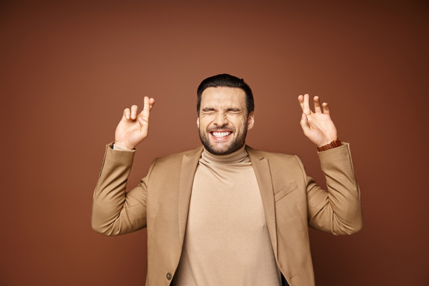 portret atrakcyjnego mężczyzny w eleganckim stroju uśmiechniętym palcami na beżowym tle - Zdjęcie, obraz