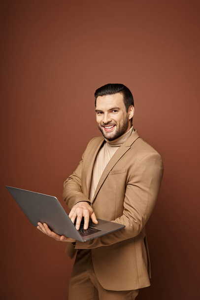 alegre y guapo profesional usando su portátil mientras trabaja remotamente sobre fondo beige - Foto, imagen