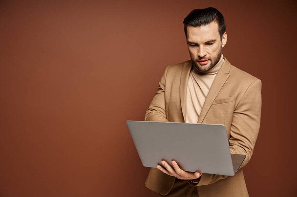profesional enfocado y guapo usando su computadora portátil mientras trabaja remotamente sobre fondo beige - Foto, imagen