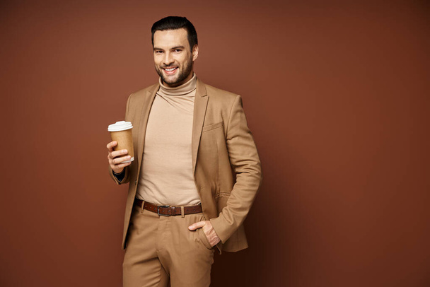 boldog férfi elegáns öltözékben kezében kávé menni, és állva kéz a zsebben bézs háttér - Fotó, kép