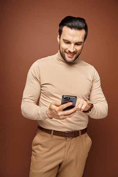 happy man with bristle in turtleneck using his smartphone on beige background, social media - Photo, Image