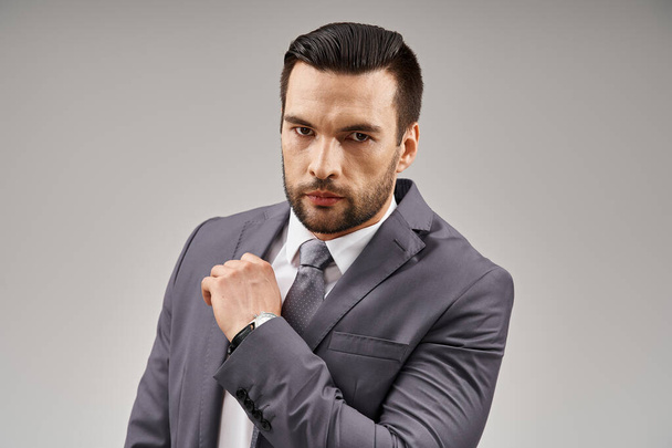 intense gaze from a handsome man with bristle posing in a grey suit on light background in studio - Photo, Image