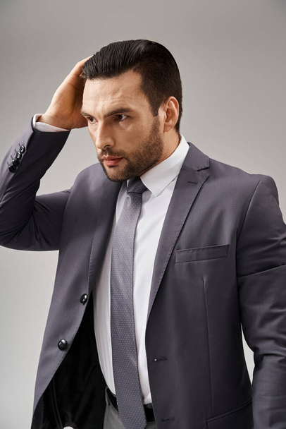 hombre guapo en ropa formal con corbata ajustando su cabello sobre fondo gris, moda corporativa - Foto, Imagen