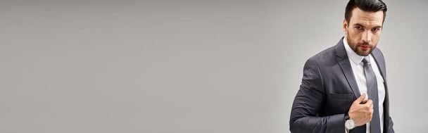 Empresário carismático de terno com uma postura confiante olhando para a câmera em fundo cinza, banner - Foto, Imagem