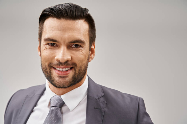 портрет веселого бизнесмена в стильном наряде, позирующем на сером фоне, с индивидуальным костюмом - Фото, изображение