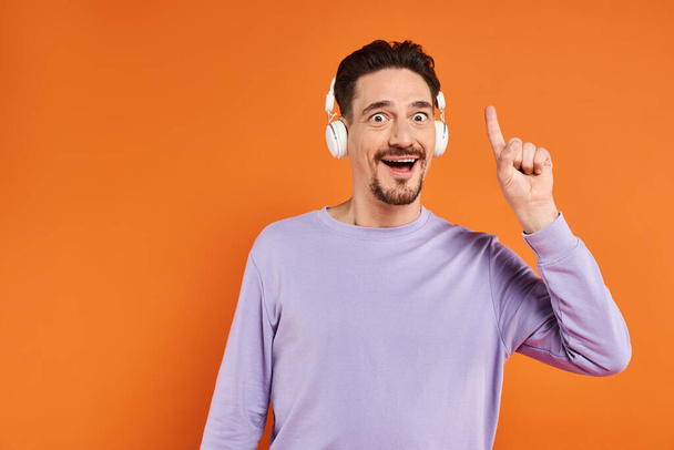amazed bearded man in wireless headphones listening music on orange background, idea gesture - Photo, Image