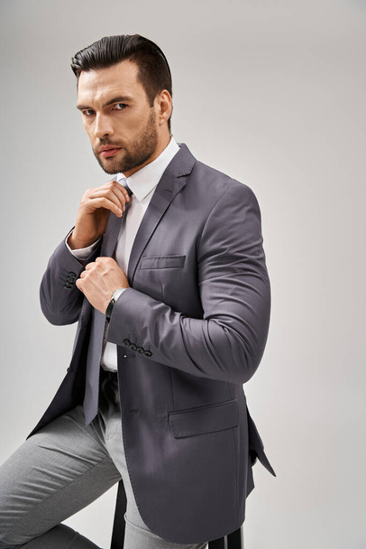 pensativo hombre de negocios en traje ajustando su corbata sobre fondo gris, concepto de estilo corporativo - Foto, imagen