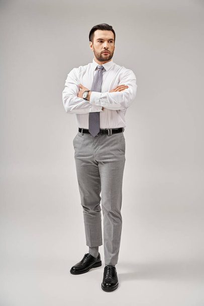 intera lunghezza di uomo d'affari in abito in piedi con le braccia incrociate mentre posa su sfondo grigio - Foto, immagini