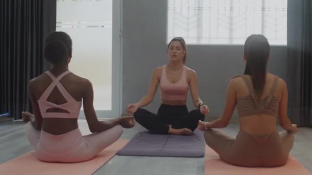 Mediana oportunidad de instructora de yoga femenina haciendo asana con mujeres durante la meditación en clase de yoga en un amplio estudio - Metraje, vídeo