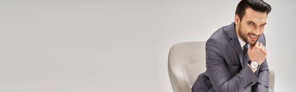 portret szczęśliwego biznesmena w eleganckim garniturze siedzącego na wygodnym fotelu na szarym tle, baner - Zdjęcie, obraz