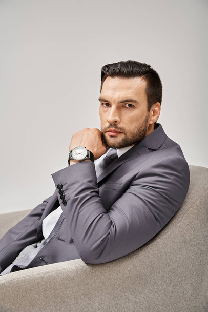 portrét dobře oblečeného podnikatele v elegantním obleku sedícího na pohodlném křesle na šedém pozadí - Fotografie, Obrázek
