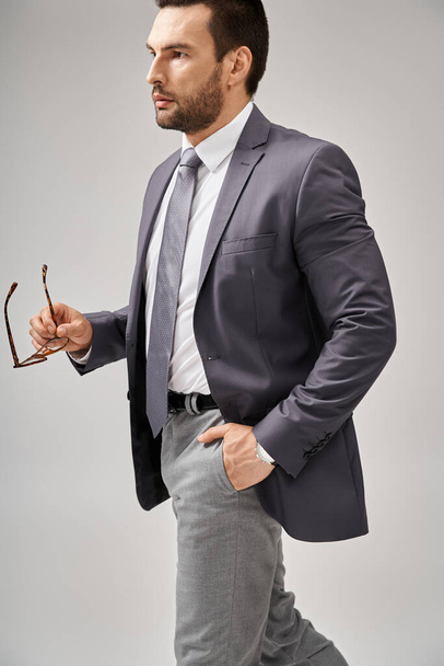 フォーマルウェアの自信を持ったビジネスマンはグレーのポケットに手をつないでメガネを握り,立っています - 写真・画像