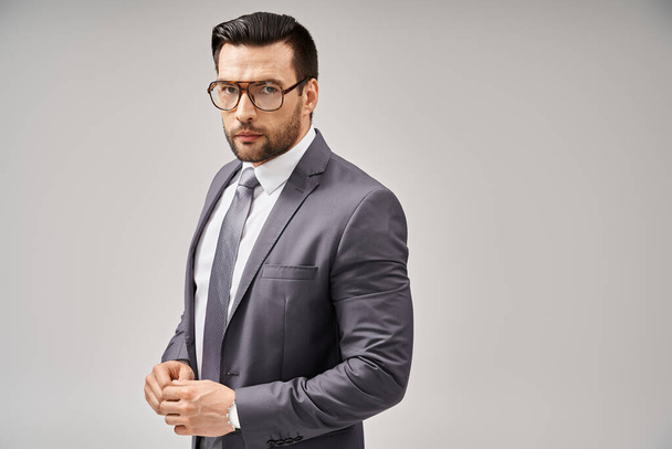 hombre de negocios guapo en ropa formal y gafas de pie sobre fondo gris, elegancia y estilo - Foto, imagen