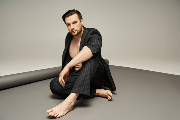 homem elegante e bonito com peito nu e pés posando em terno pinstripe no fundo cinza - Foto, Imagem