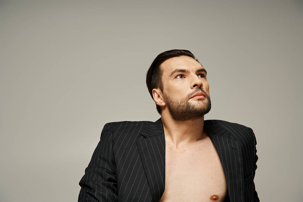 портрет стильного и красивого мужчины с обнаженной грудью, позирующего в полосатом костюме на сером фоне - Фото, изображение