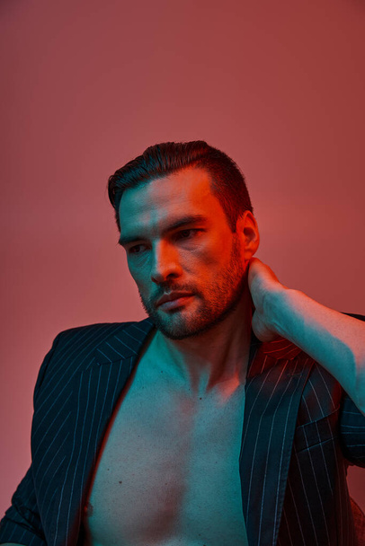 portrait of man with bare chest posing in elegant pinstripe suit in studio with red and blue light - Photo, Image