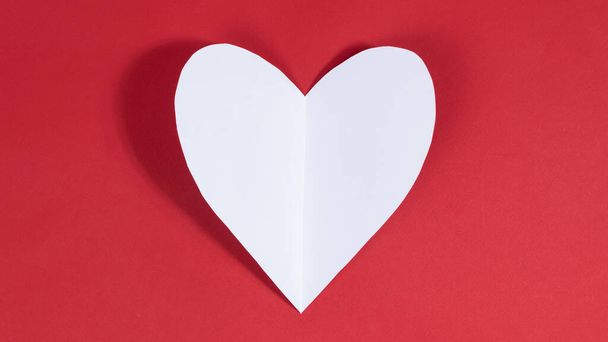 Big white heart on red background. Symbol of love. Greeting card. Concept of valentine's holiday, wedding and other occasions to express love. Copy space. Flat lay. - Valokuva, kuva