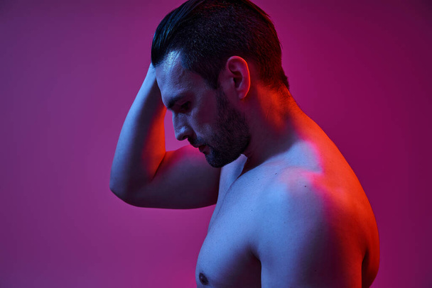 sexy e muscoloso uomo con setola posa con mano vicino testa su sfondo viola, vista laterale - Foto, immagini
