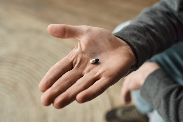 vista ritagliata dell'uomo che tiene la capsula blu e bianca, foto ravvicinata del farmaco in mano maschile - Foto, immagini